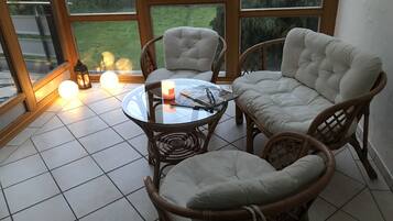Un coin salon accueillant avec des fauteuils en osier et une table en verre, agrémenté d’une bougie et d’un livre.