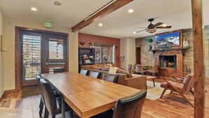 A spacious dining area with a long wooden table and comfortable seating, a fireplace, and a television mounted above it. - Rooftop Hot Tub After the Slopes (Park City)