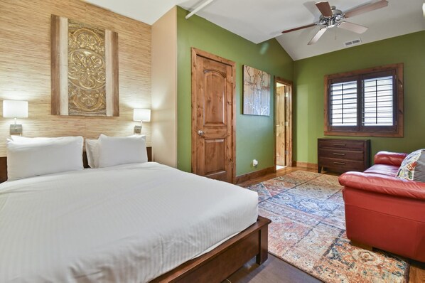 A bedroom with a large bed, a red sofa, a wooden door, and a ceiling fan.