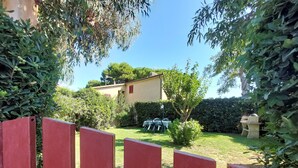 Un jardín vallado con una casa al fondo, un árbol pequeño y una mesa con sillas.
