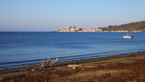 Vista costera con playa, un barco pequeño y un pueblo lejano.