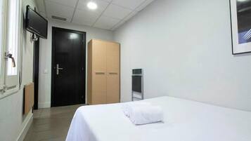 Quarto de hotel com cama, televisão, guarda-roupa e porta.