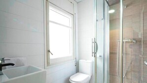Un baño con ducha de vidrio, inodoro blanco y un lavamanos grande.