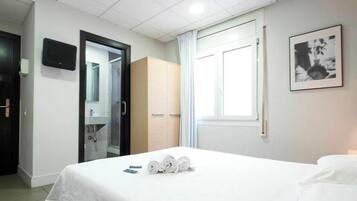 Una habitación de hotel con cama, armario, baño con espejo y un cuadro en la pared.