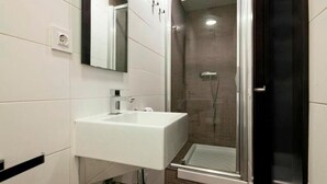 Un baño moderno con lavamanos blanco, un espejo y una zona de ducha con mampara de vidrio.