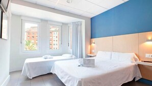 Habitación de hotel con dos camas, un ventanal con cortinas, pared de acento azul y vista a edificios.