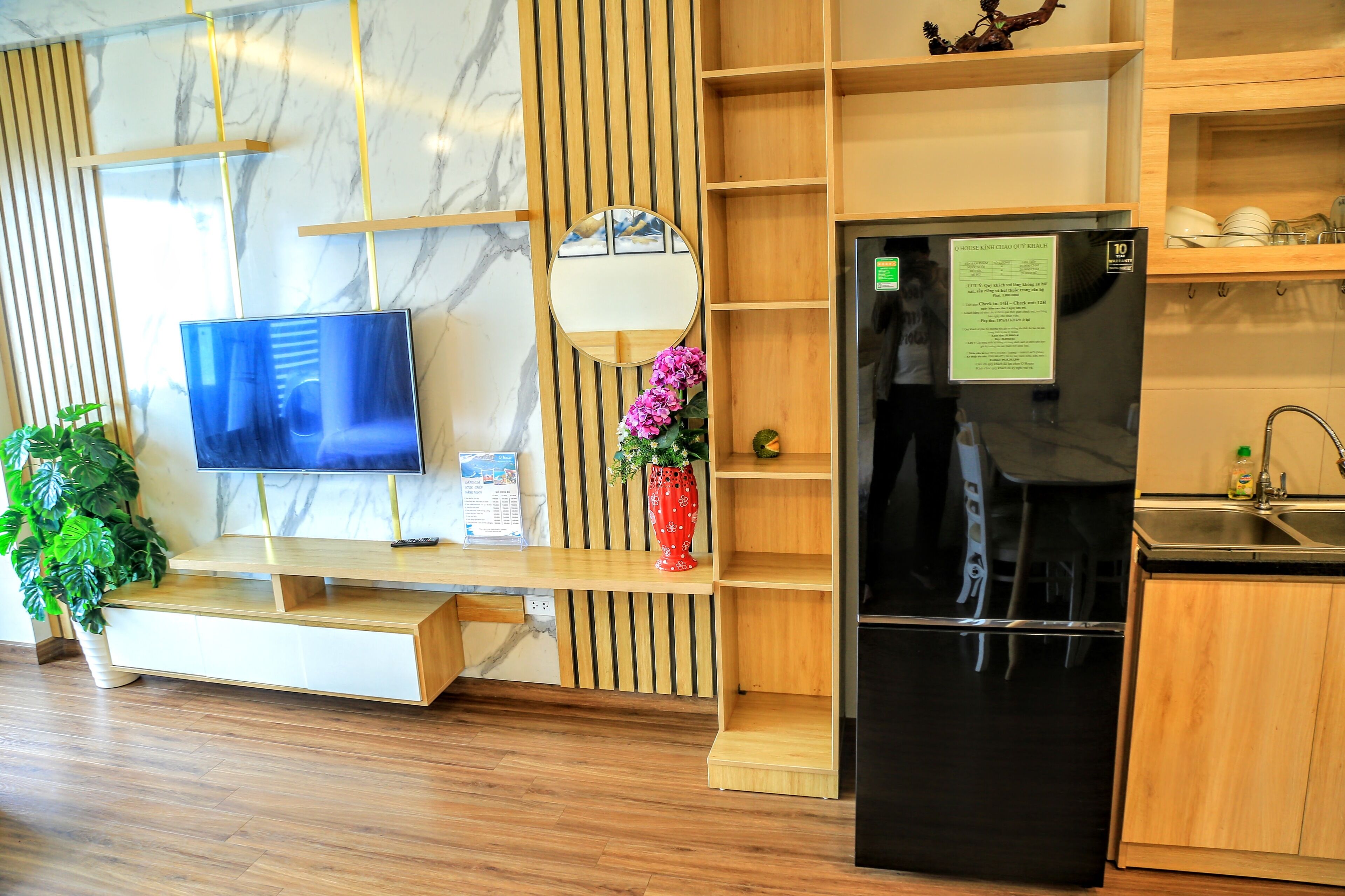 A modern kitchen with a black refrigerator, wooden shelves, a TV, and a potted plant.