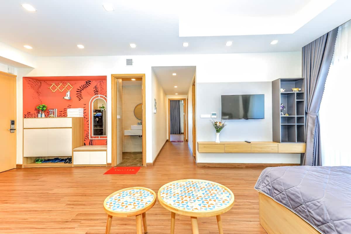 A modern hotel room with a wooden floor, a bed, a TV, a desk, and a small seating area.