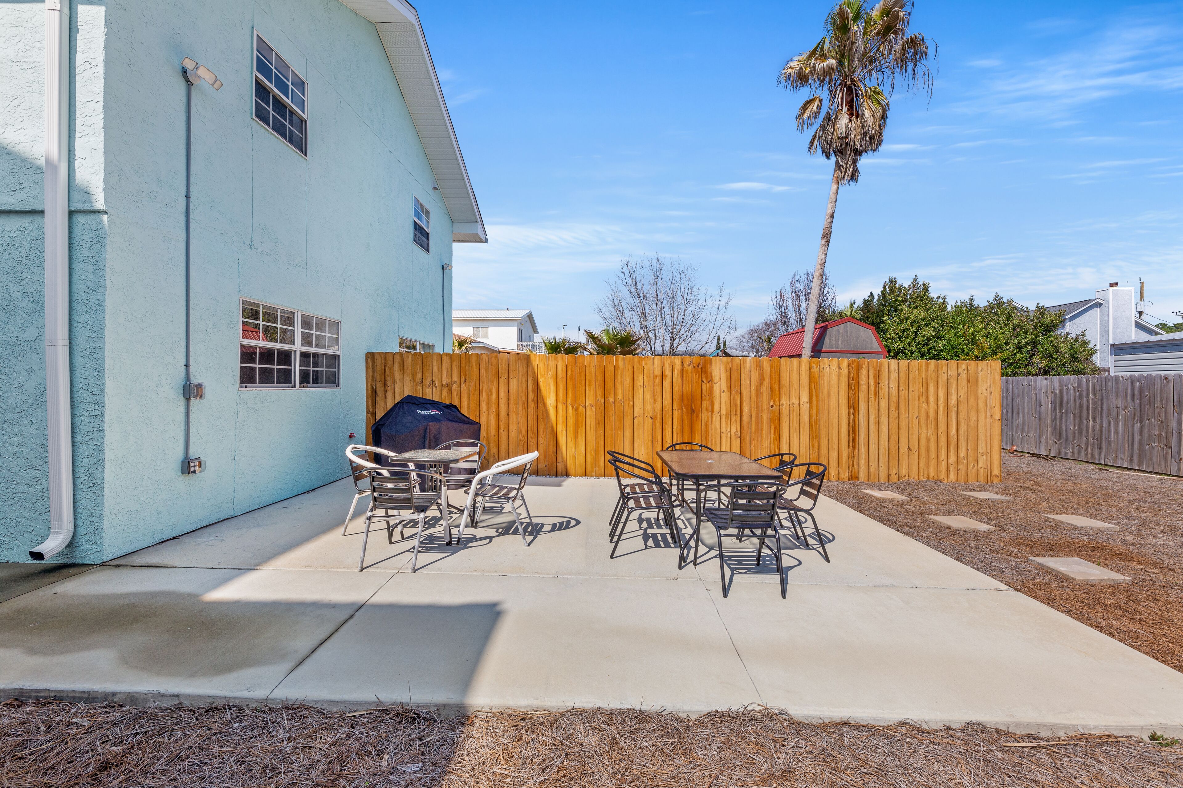 Une terrasse à l’arrière de la maison, avec une table et des chaises, une clôture en bois et un palmier.