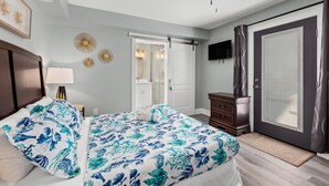 Un dormitorio con cama, mesita de noche, cómoda, ventilador de techo, televisor y puerta corrediza de vidrio.