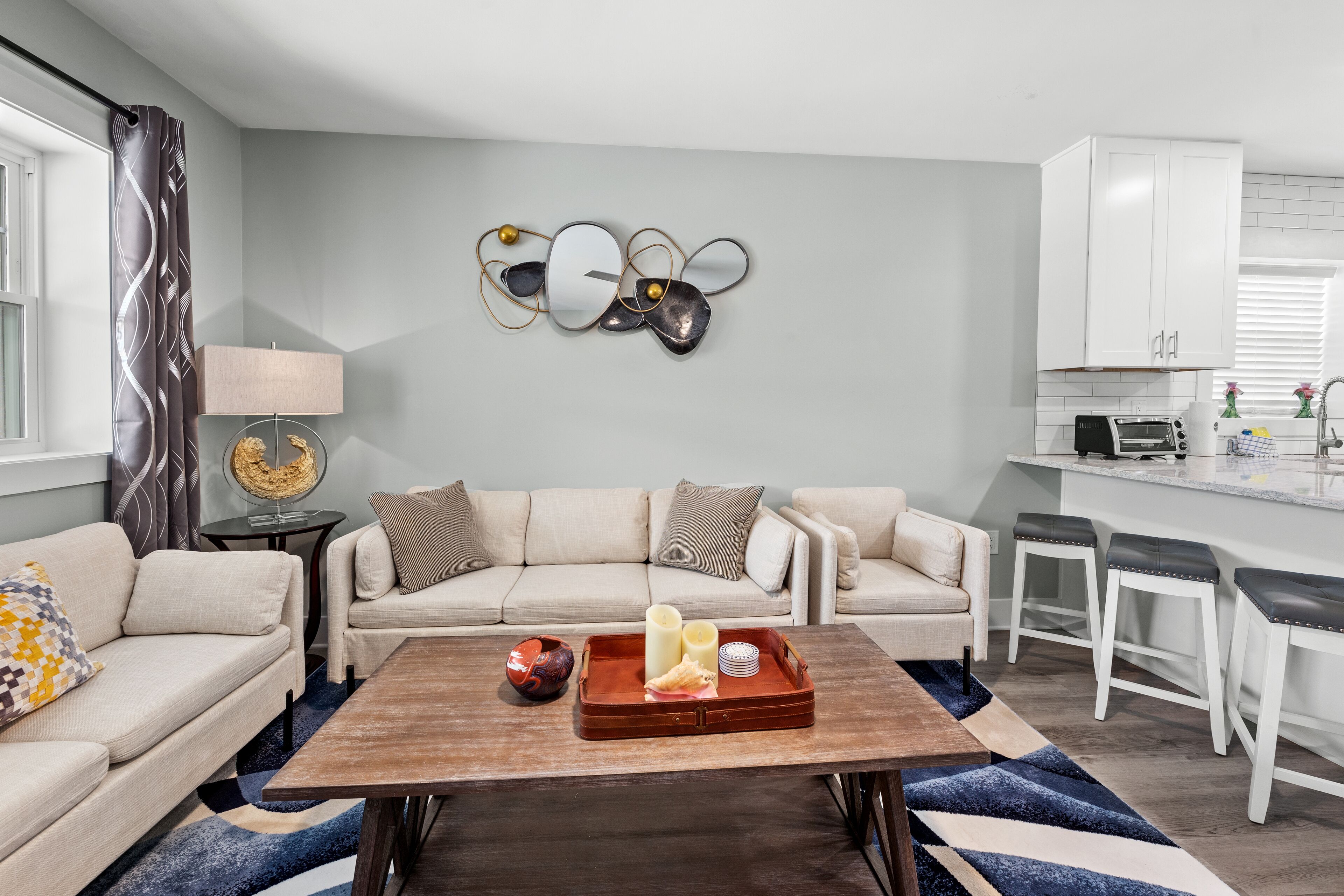 A modern living room with a sofa, a coffee table with a tray, and a kitchen area with white cabinets and a countertop.