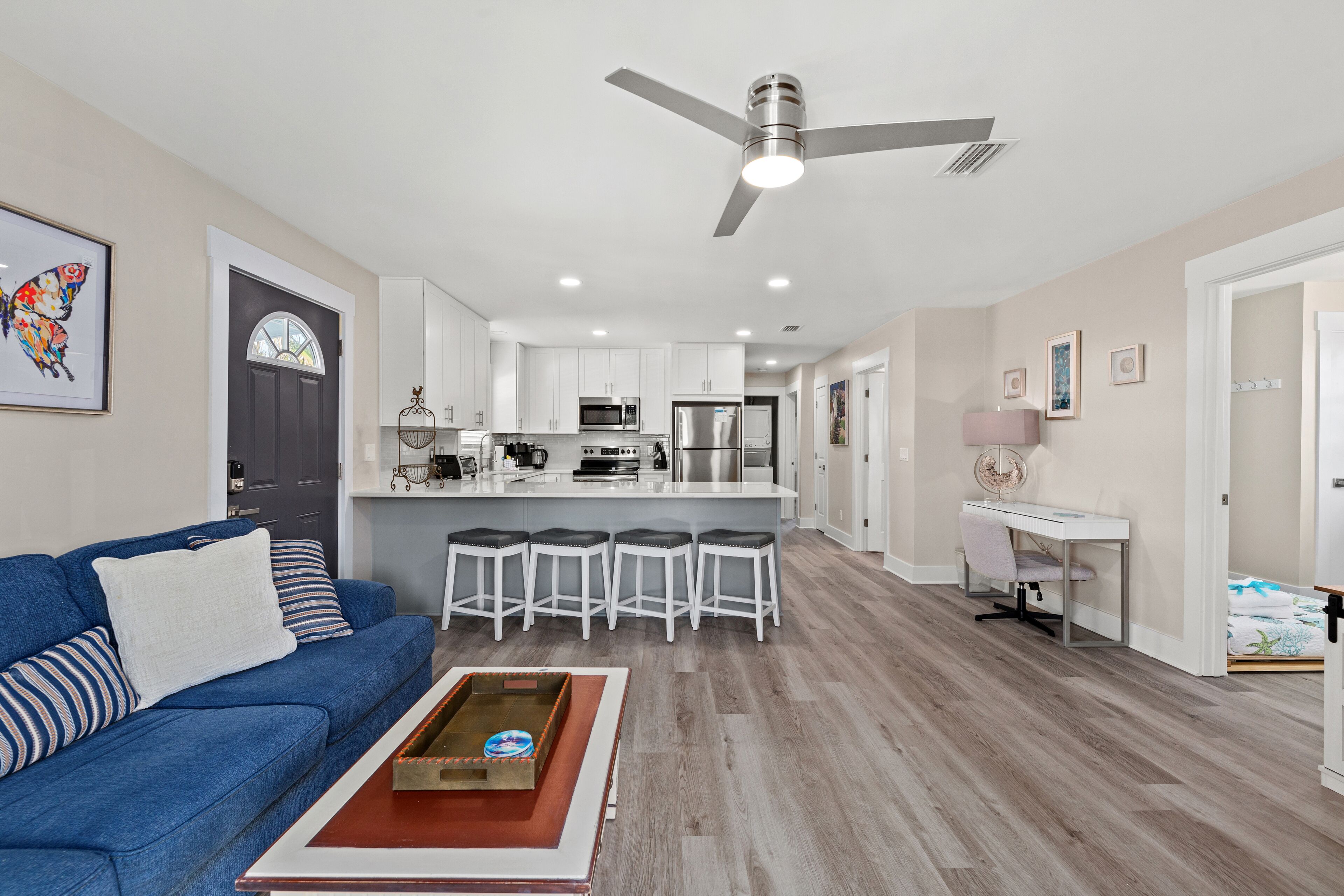 Una sala de estar moderna con un sofá azul, una mesa de centro y una zona de cocina con armarios blancos e una isla central.