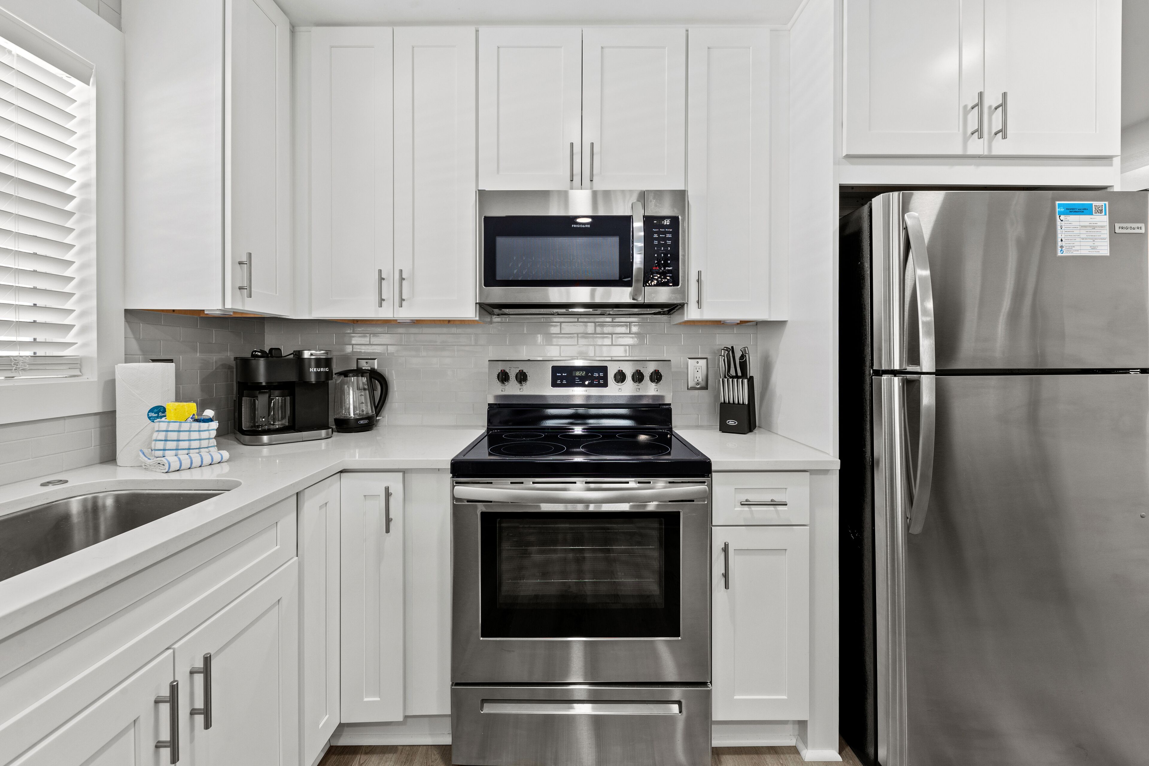 A modern kitchen with white cabinets, a stainless steel refrigerator, a built-in microwave, a stove, and a coffee maker.