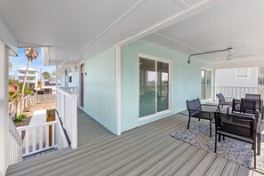 A covered outdoor area with a wooden deck, a seating area with chairs and a table, and a sliding glass door leading to a covered patio. - Welcome to Dolphin Fun B, Brand NEW Duplex Walk to the Beach (Panama City Beach)