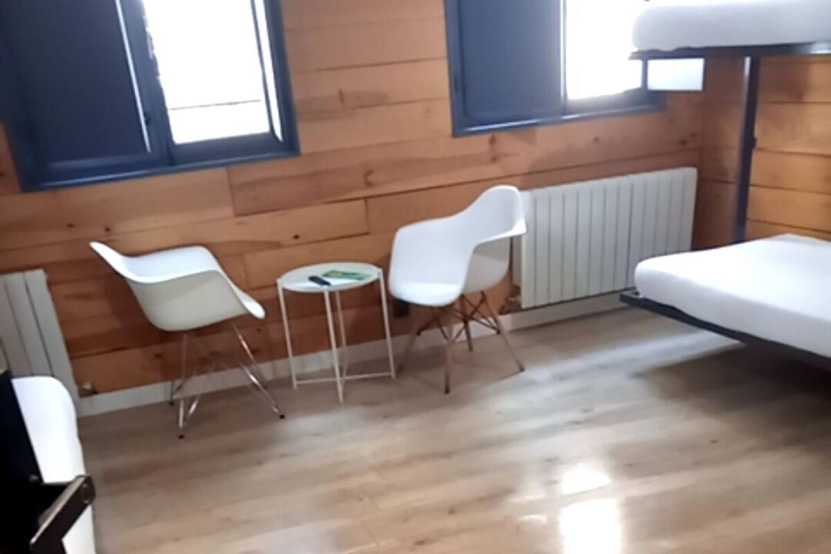 Une pièce avec un plancher en bois, un lit blanc, deux chaises blanches et une petite table ronde.