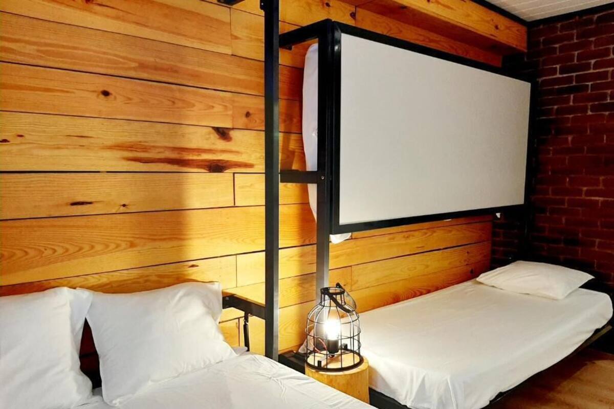 Une chambre avec deux lits simples, un mur en bois, un mur en briques et une tête de lit en métal.
