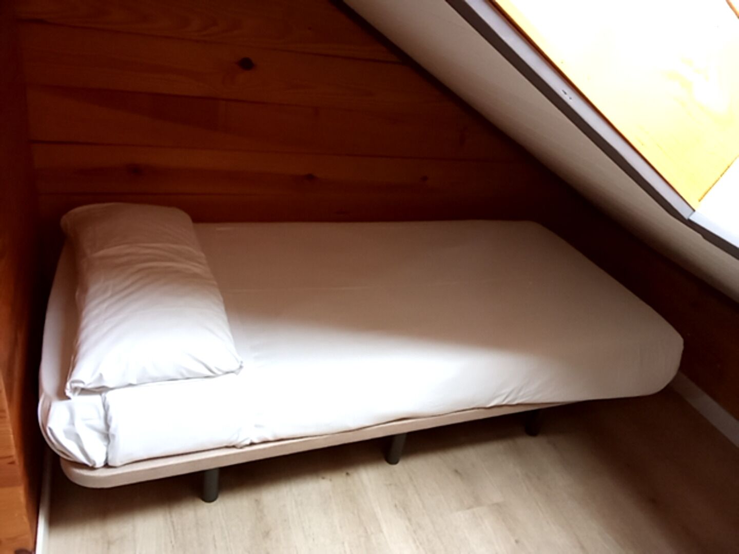 A small, single-bed room with a wooden ceiling and a window.