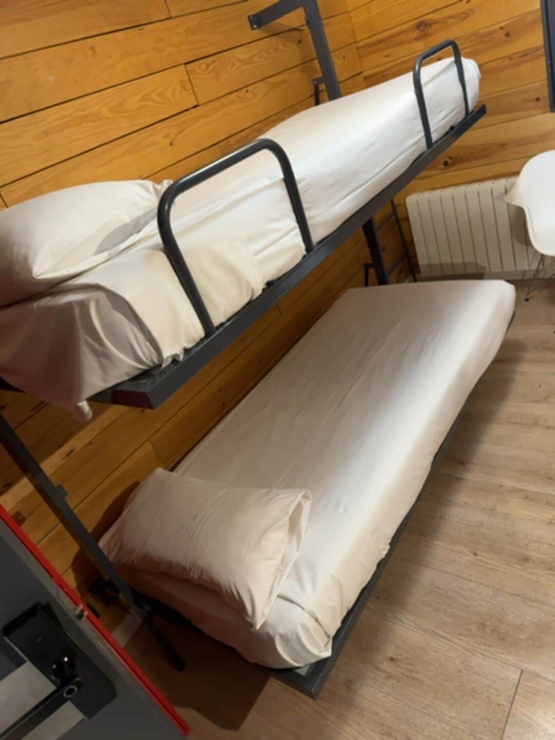 A bunk bed with a mattress and pillows, a radiator, and a chair.