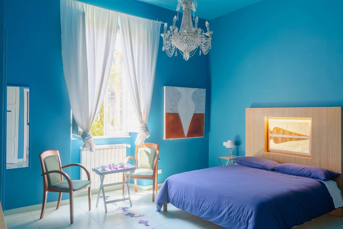 A bedroom with a large bed, two chairs, a table, and a window with curtains.