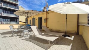 Une terrasse sur le toit, avec des chaises longues, une table et des parasols.
