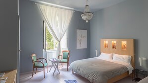Une chambre avec un grand lit, un lustre, une fenêtre avec des rideaux et un fauteuil.