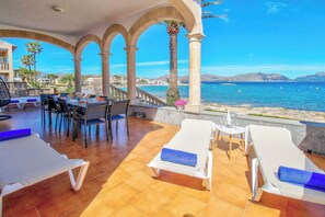 A sunlit outdoor seating area with lounge chairs and a table, overlooking a coastal view. - Cas Siulet by Rentallorca (Alcúdia)