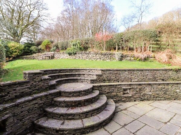 A stone staircase leading up to a stone wall, surrounded by a well-maintained garden with a lawn and various shrubs.