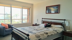 Una camera da letto con un letto, una sedia, un comodino, una lampada e una finestra vista palme.