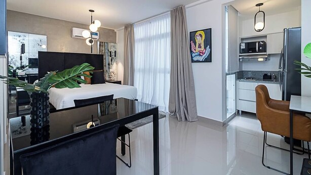 Une chambre d’hôtel moderne équipée d’un lit, d’un bureau avec une chaise, d’une table à manger et d’une kitchenette.
