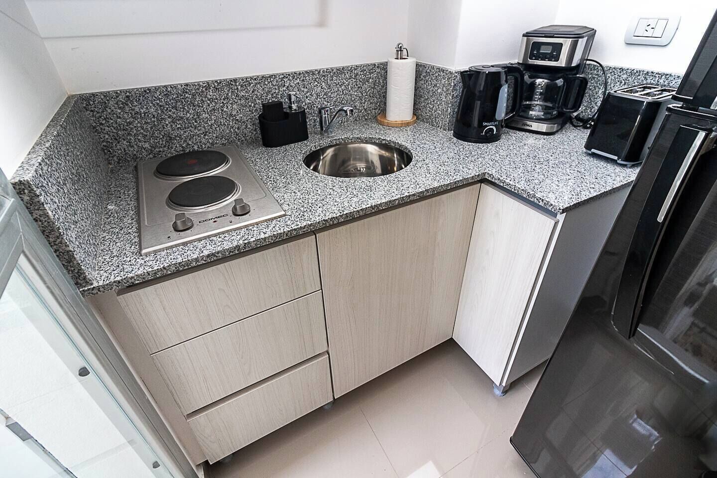 A compact kitchen with a granite countertop, stainless steel sink, a coffee maker, and a toaster.