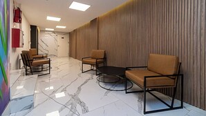 Um hall moderno com piso de mármore, balcão de recepção e áreas de estar com sofás e poltronas.
