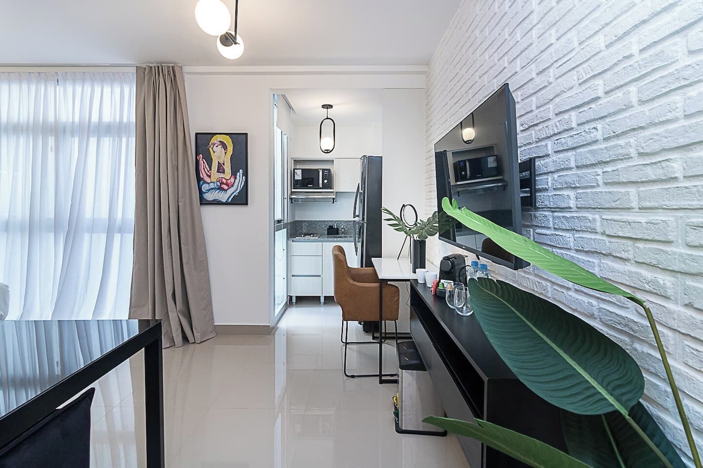Une cuisine moderne équipée d’un téléviseur à écran plat, d’un coin repas avec une table et des chaises, et d’un salon agrémenté d’une grande plante.