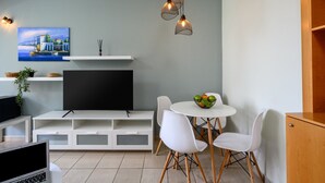Een moderne woonkamer met een flatscreen televisie, witte meubels, een eettafel met stoelen en een schilderij aan de muur.