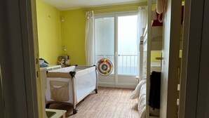 A room with a bed, a bedside table, a window with curtains, and a door. - Calm sea view family appartment in historical town center (Villers-sur-Mer)