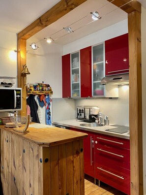 A kitchen with wooden beams, red cabinets, a wooden island, and a microwave.
