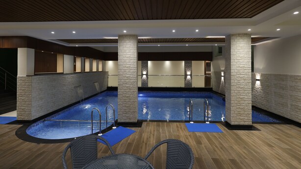 An indoor swimming pool with stone pillars, blue mats, and wicker chairs. - Pride Biznotel Canopus Digha (Kanthi)