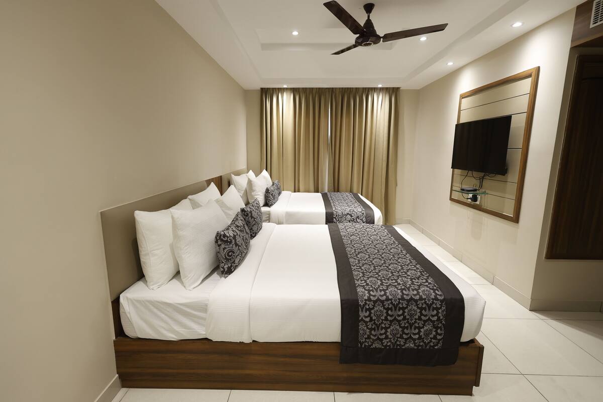 Une chambre d’hôtel avec un grand lit, un ventilateur de plafond, un téléviseur fixé au mur et une fenêtre avec des rideaux.