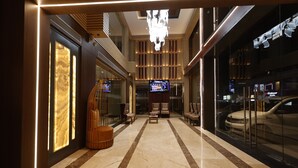 A modern hotel lobby with a marble floor, seating area, and a large TV screen. - Pride Biznotel Canopus Digha (Kanthi)