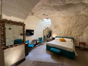 A bedroom with a large bed, a sitting area with chairs, a television, and a mirror. - L'antica Conceria (Matera)
