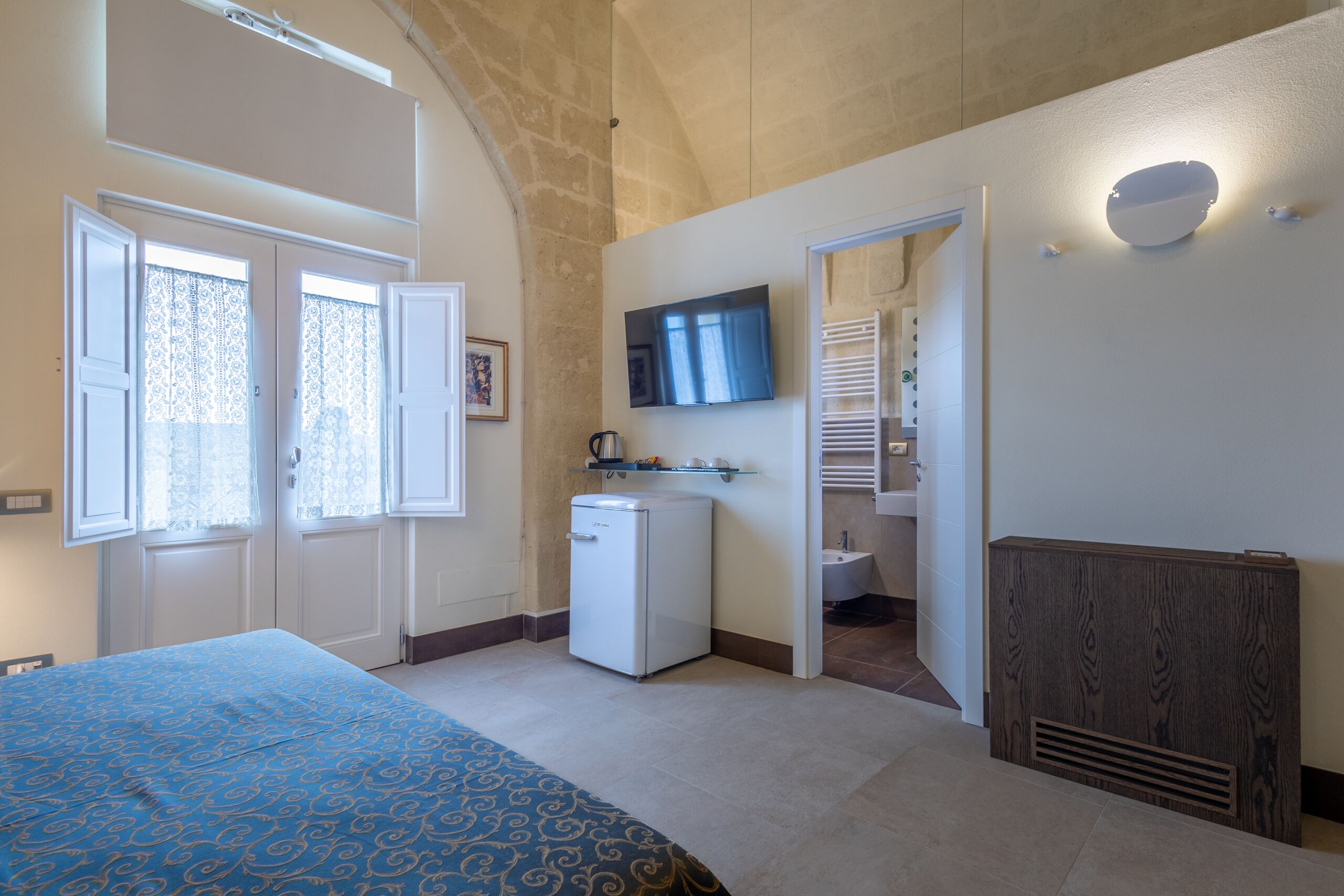 Une chambre avec un lit, un petit coin cuisine, une télévision et une salle de bain visible à travers une porte ouverte.