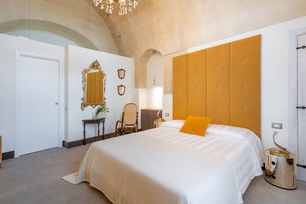 A hotel room with a large bed, a wooden headboard, a mirror, a chair, and a bedside table.