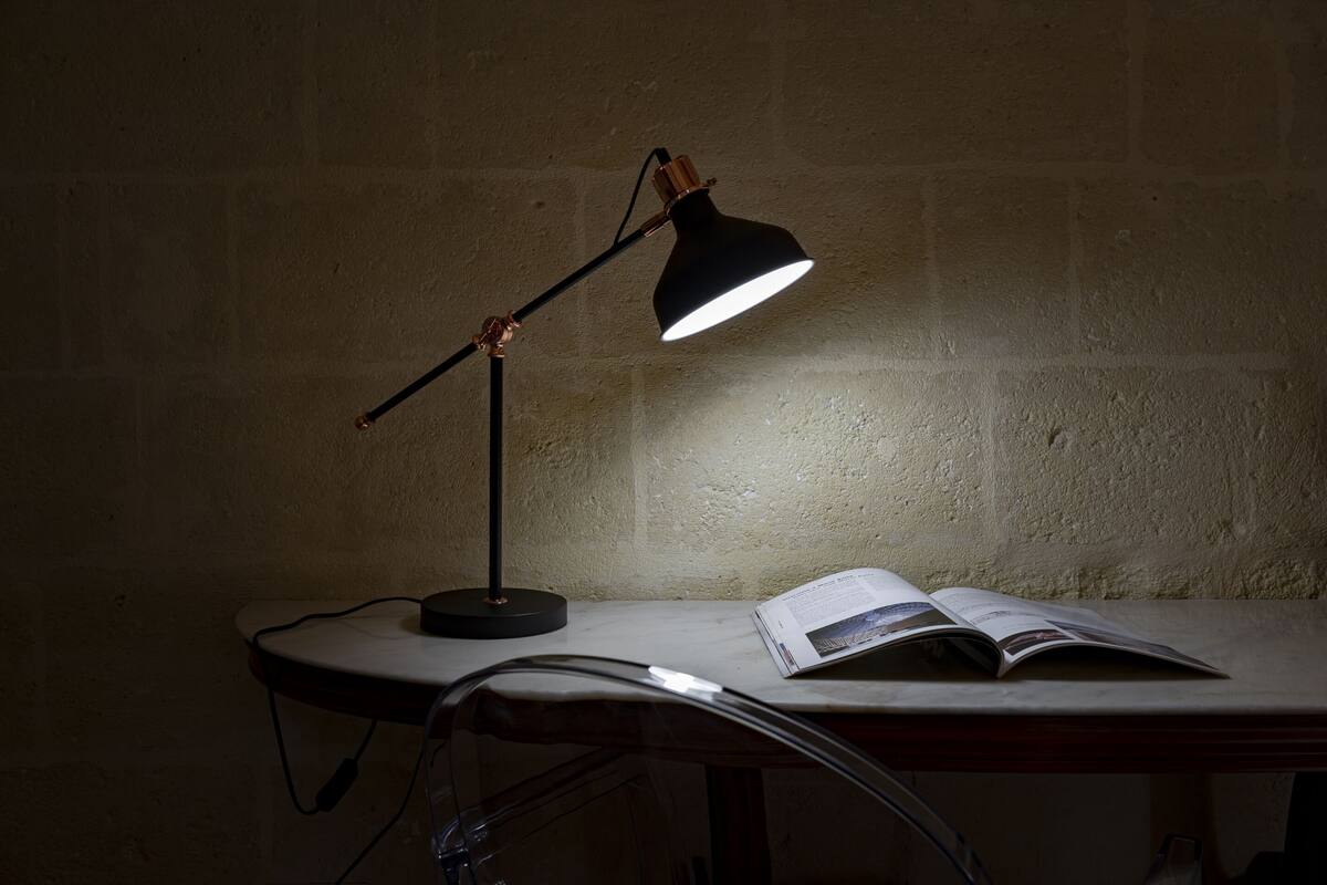 A desk with a lamp, an open book, and a chair.