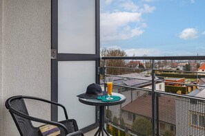 A balcony with a chair, a small table with a drink and a hat, and a view of buildings. - Studio with Balcony in Sarbinowo | Only 170 m to the Beach (Sarbinowo)