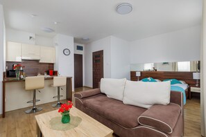 A modern hotel room with a kitchenette, a brown sofa, a wooden coffee table with flowers, and a bed with blue bedding. - Studio with Balcony in Sarbinowo | Only 170 m to the Beach (Sarbinowo)