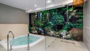 A modern bathroom with a glass-enclosed jacuzzi, a waterfall mural, and a wooden bucket.