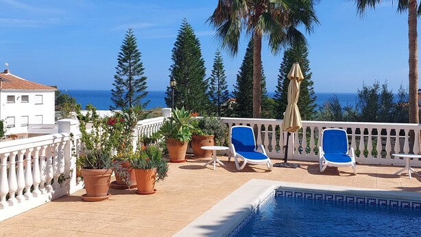 Zona junto a la piscina con sillones, plantas en macetas y vista al mar.