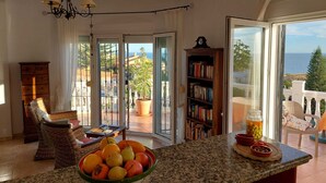 Amplia sala de estar con un ventanal que ofrece vista al mar, un comedor con fruteros y una estantería.