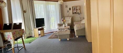A cozy living room with a wooden ceiling, a television, a sofa set, and a dining area with a table and chairs.