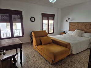 A bedroom with a bed, a sofa, a nightstand, a mirror, and a window with blinds.