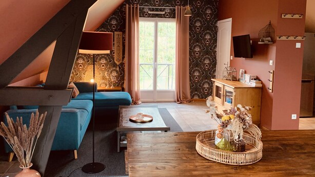 Un salon chaleureux de style loft, doté d’un plafond en pente, d’un canapé bleu, d’une table basse en bois et d’un vase décoratif contenant des fleurs séchées.